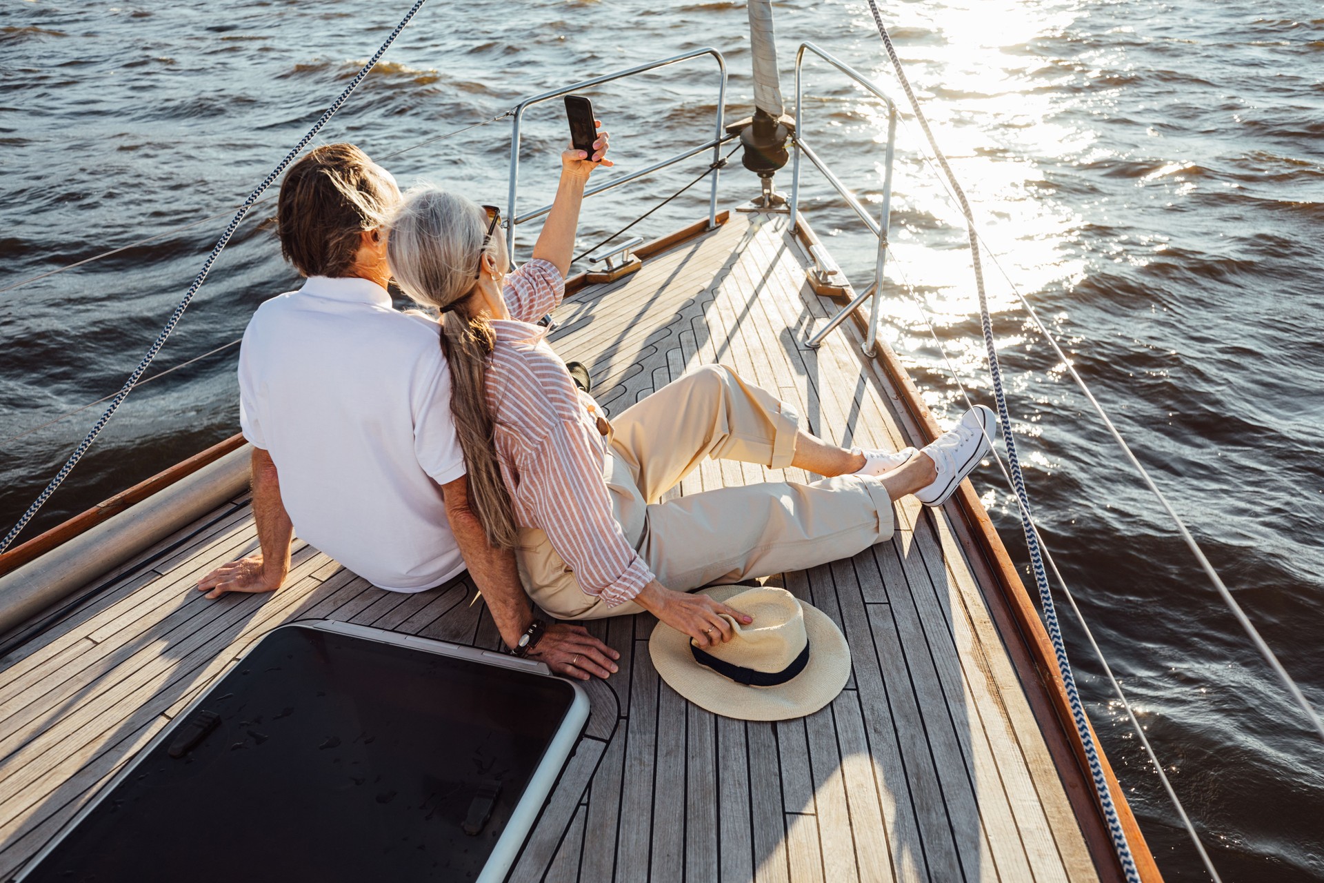 Two senior people sitting together on a yacht bow and taking selfie. Mature couple taking photographs on mobile phone during a boat trip.